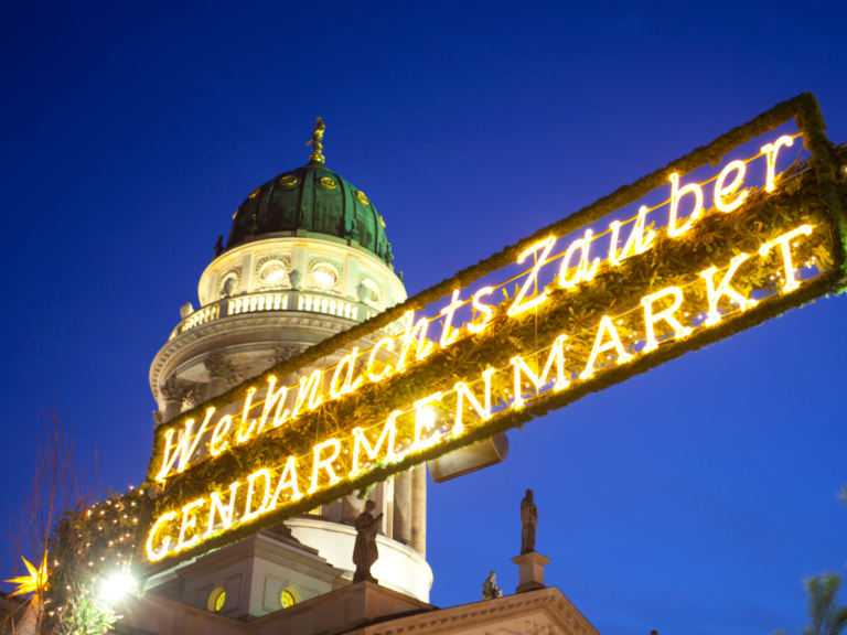 Magical lights and building landscape at the entrance of Christmas Market. The sign is made of lights and reads WelhnachtsZauber Gendarmenmarket.