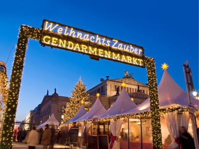 Magical lights and vendor tents at the entrance of Christmas Market. The sign is made of lights and reads WelhnachtsZauber Gendarmenmarket.
